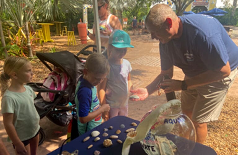 volunteer showing three kids various aquarium related items